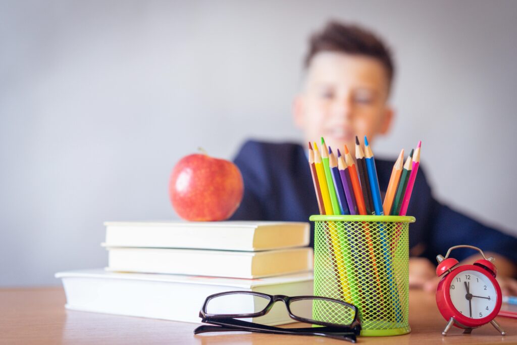 Niño con útiles escolares, libros y colores sobre la mesa, representando el inicio del aprendizaje personalizado