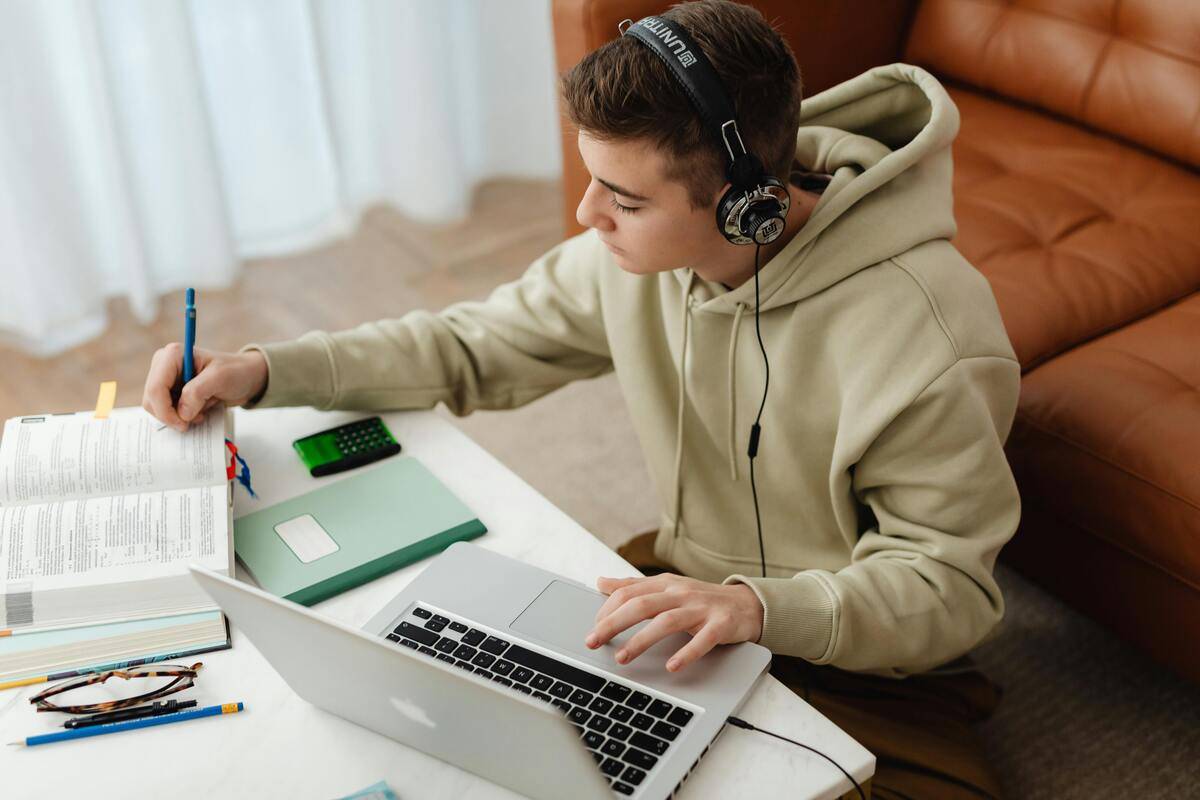 Joven estudiante con auriculares trabaja en su computadora portátil mientras toma apuntes en un cuaderno. como símbolo de la arquitectura de un LMS